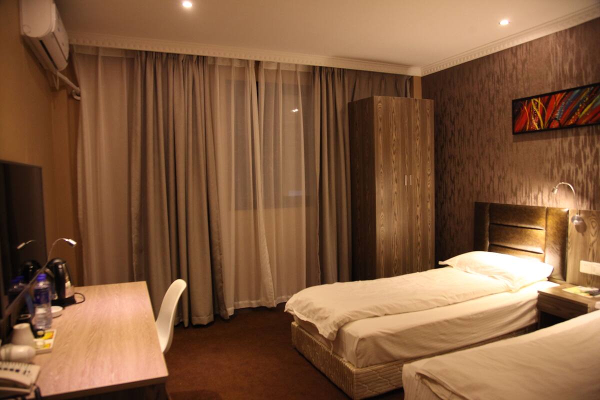 A hotel room with two beds, a desk with a chair, a TV, and an air conditioning unit.