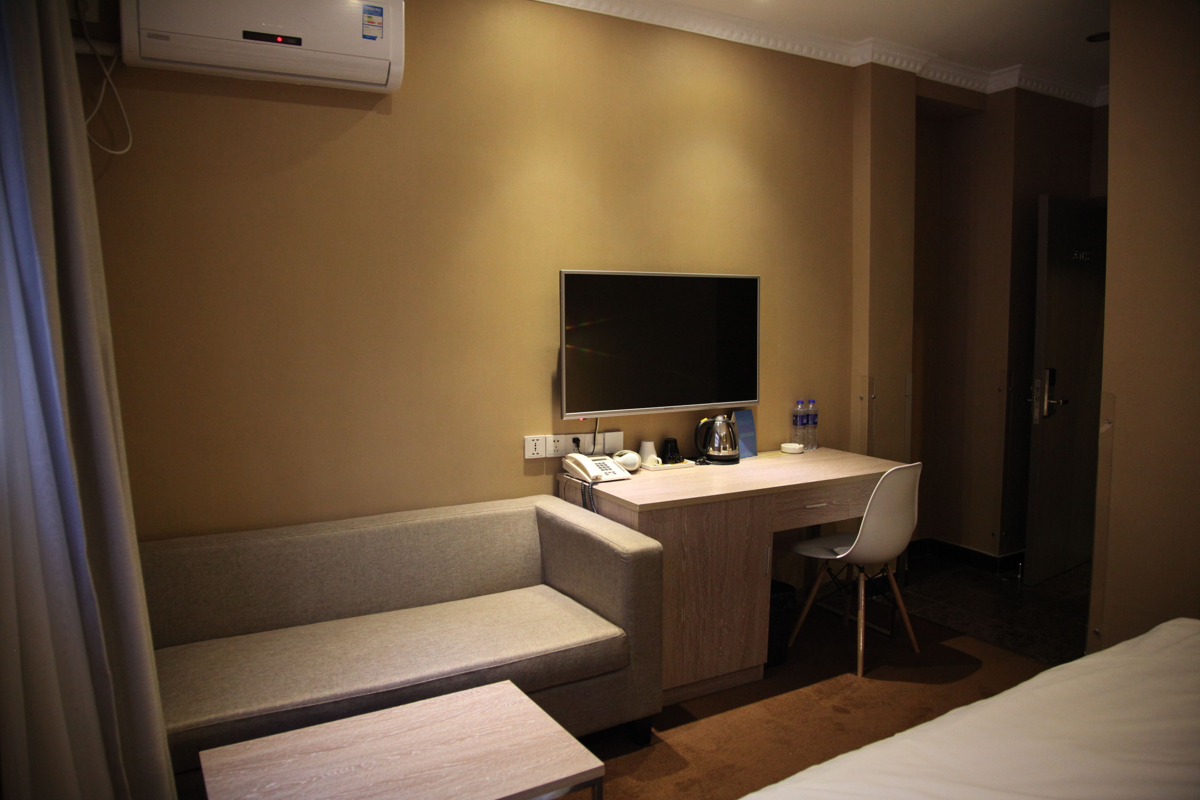 A hotel room with a sofa, a desk with a chair, a flat-screen TV, a coffee maker, and a refrigerator.