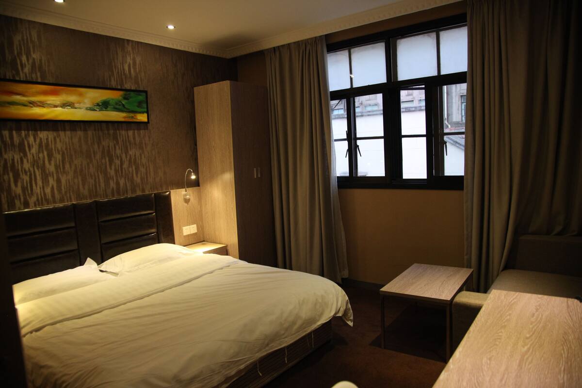 A hotel room with a bed, bedside table, and a window with curtains.