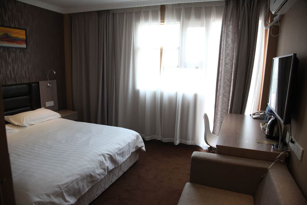 A hotel room with a bed, a desk, a chair, and a TV.