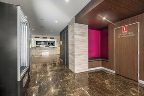 Un hall d’entrée moderne avec un sol en marbre, un comptoir d’accueil et un extincteur enroulé sur un tuyau d’incendie.