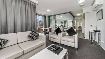 A modern hotel room with a sofa, armchairs, a coffee table, and a dining area.