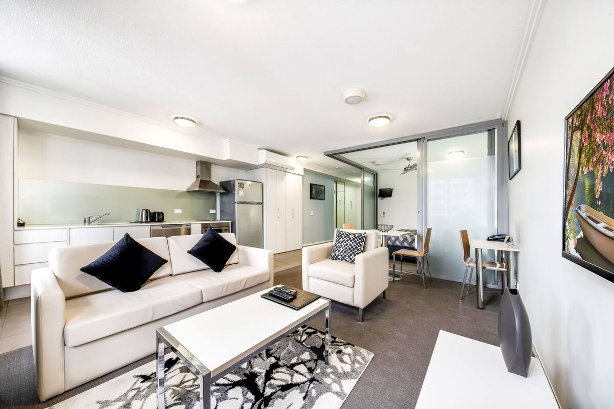 A modern living room with a white sofa, a coffee table, and a dining area with chairs and a table.