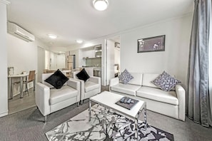 A modern living room with a sofa, armchairs, a coffee table, and a dining area. - The Capitol Apartments (South Brisbane)