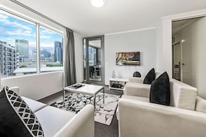 A modern living room with a sofa, coffee table, and a TV mounted on the wall. - The Capitol Apartments (South Brisbane)