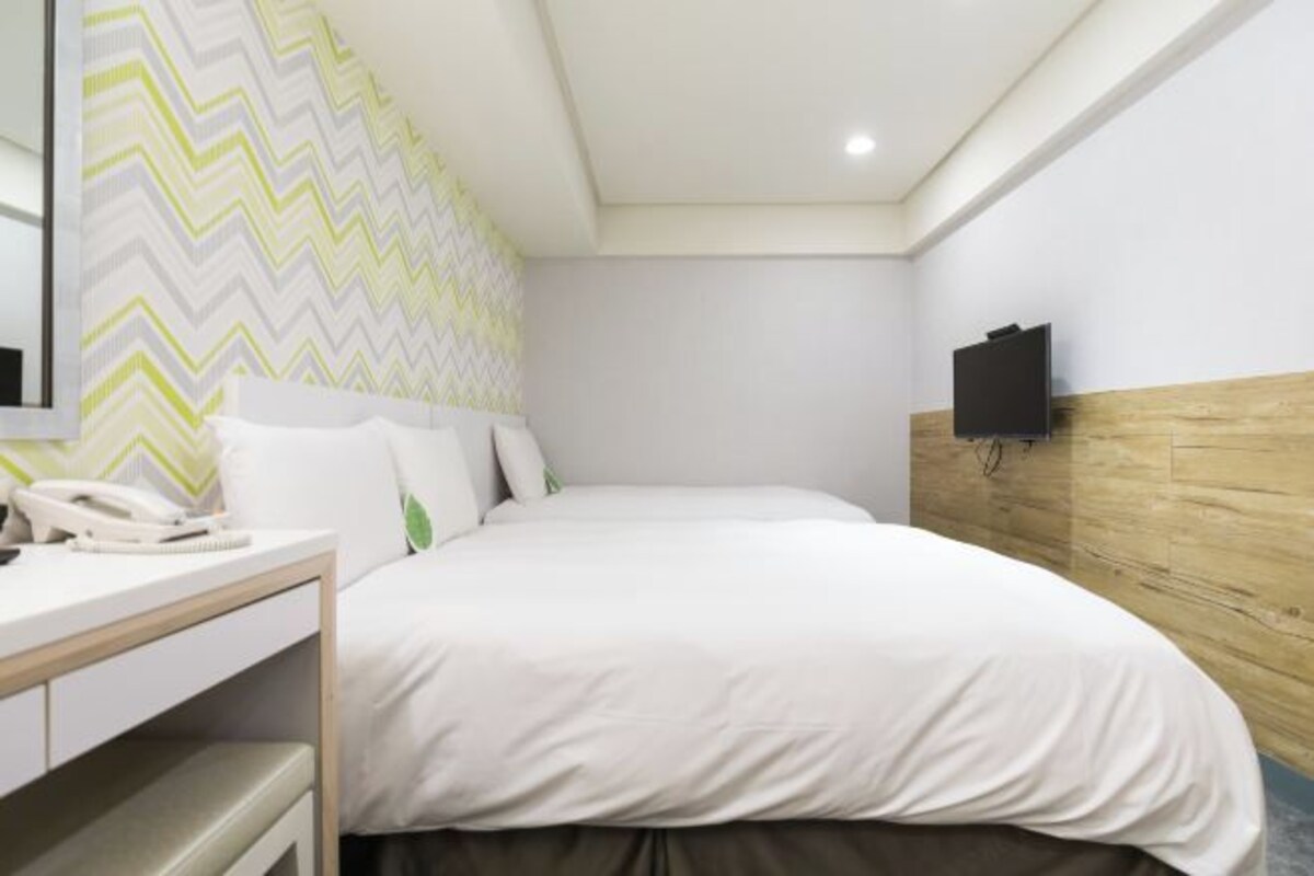 A hotel room with a bed, a bedside table with a telephone, and a wall-mounted TV.