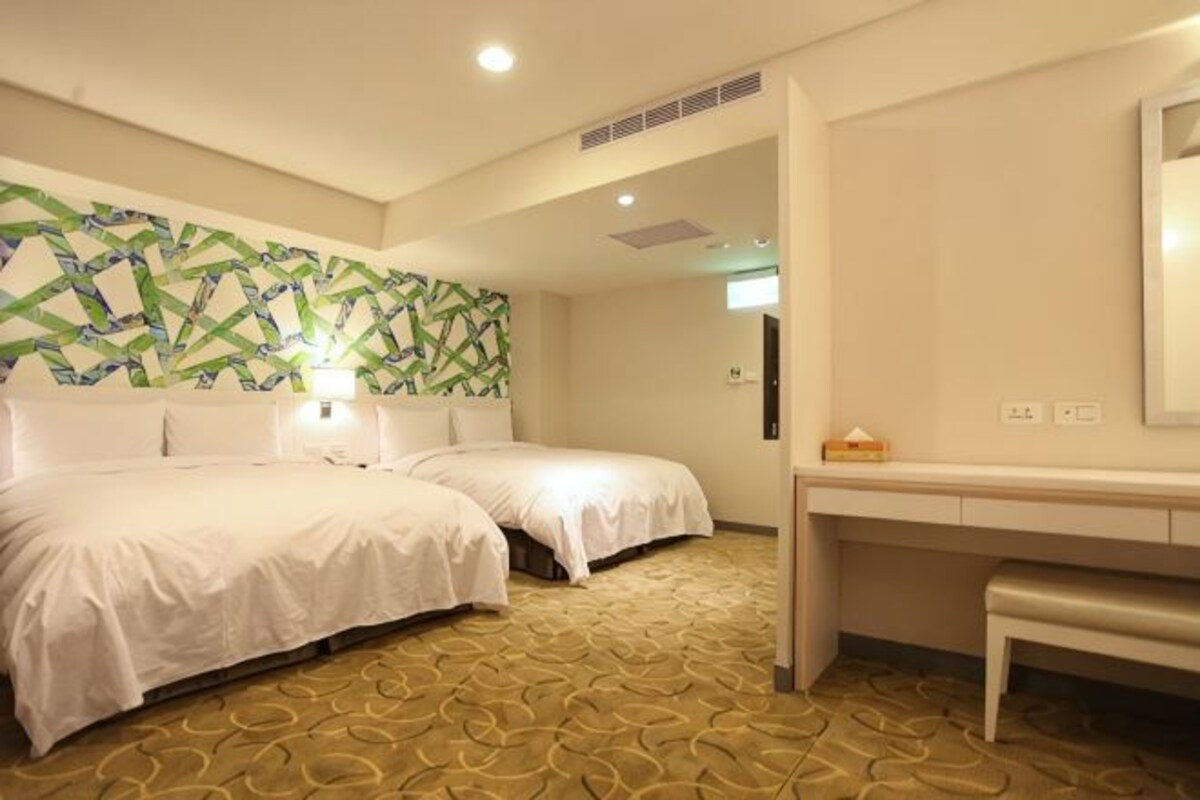 A hotel room with two beds, a desk, and a patterned carpet.