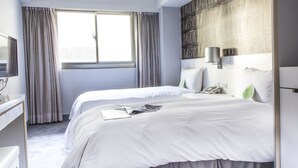 A hotel room with two beds, a large window with curtains, a bookshelf, and a bedside table with a lamp. - Ximen Citizen Hotel (Taipei)