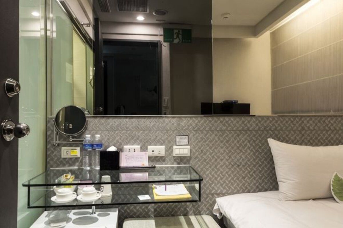 A hotel room with a glass partitioned vanity, a bed with a pillow, and a mirror.