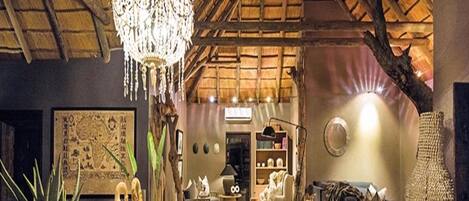 A rustic interior with a high ceiling, a chandelier, a wooden table with decorative items, a sofa, and a patterned rug.