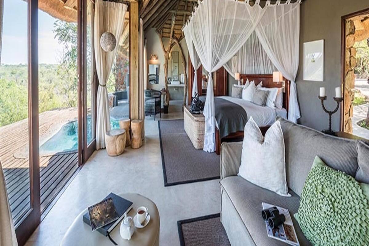 Un dormitorio con cama con dosel, una zona de estar con sofá y mesa de centro, y vistas al exterior.