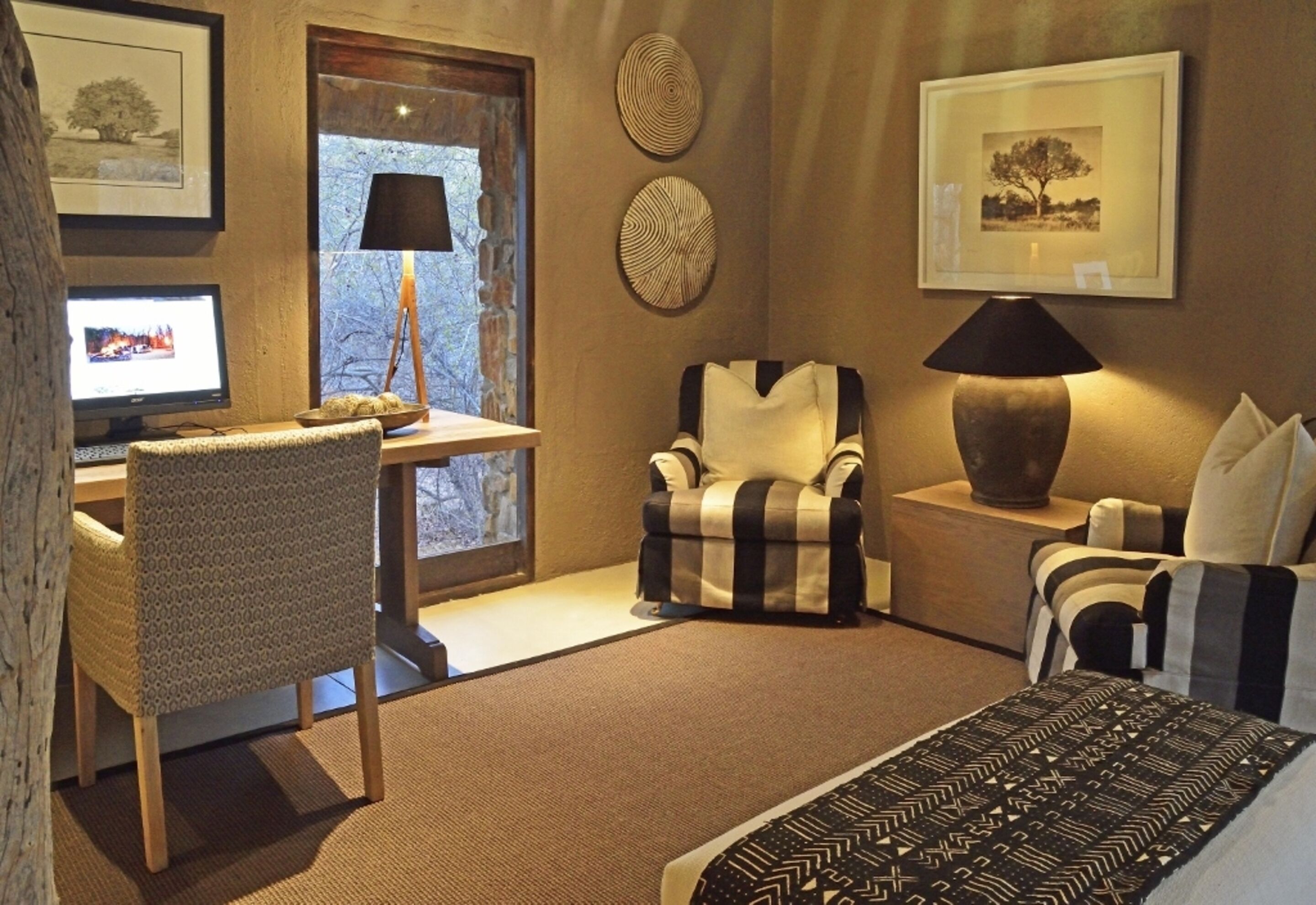 Een hotelkamer met een bureau, computer, gestreept fauteuil, bank en een bed met beddengoed met een patroon.