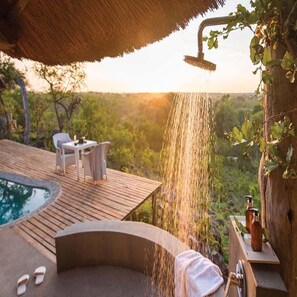 A wooden deck with a hot tub, a table with chairs, and a showerhead with water flowing. - Leopard Hills (Bushbuckridge)
