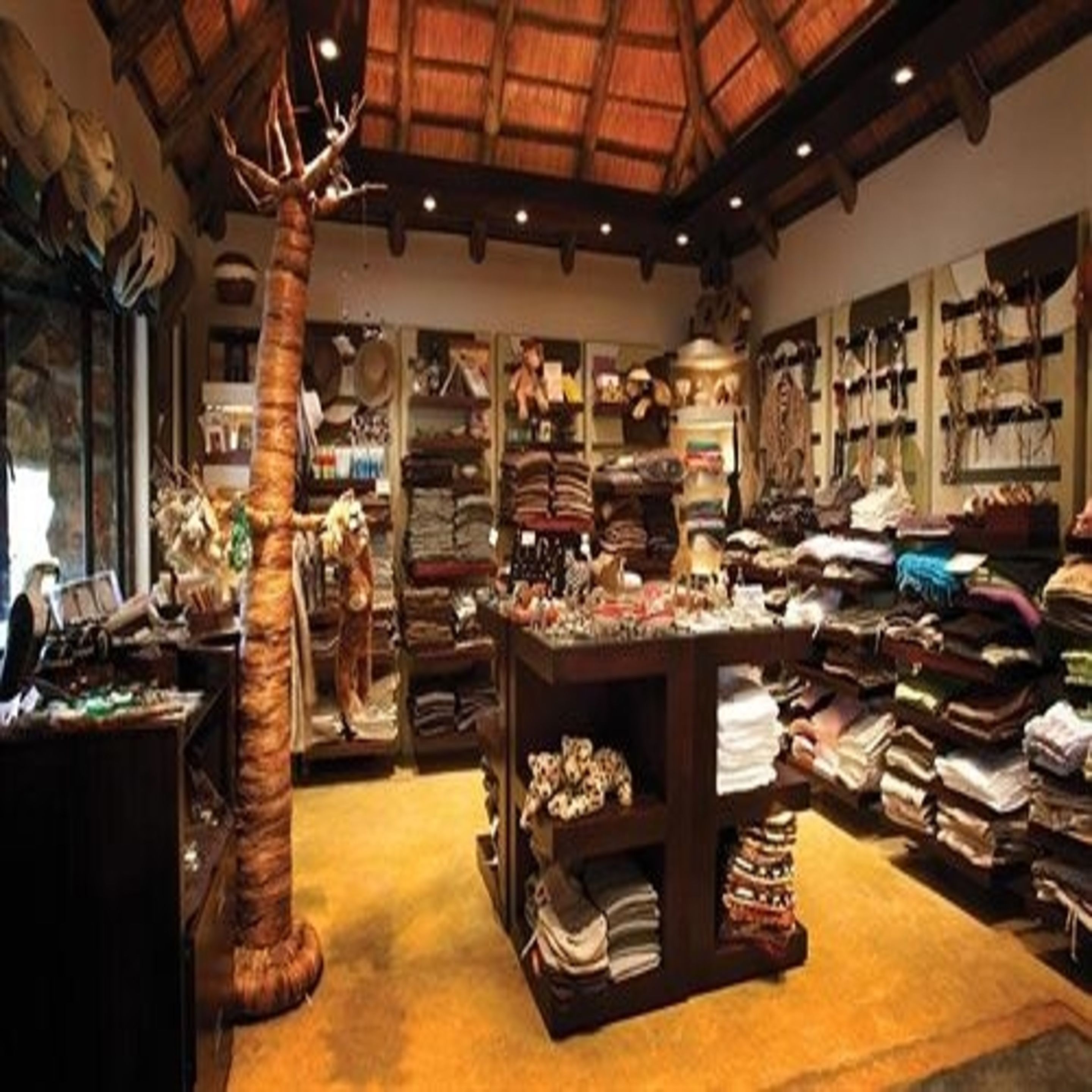 A boutique hotel interior with a central wooden table displaying various items, surrounded by shelves and racks of neatly folded clothes.