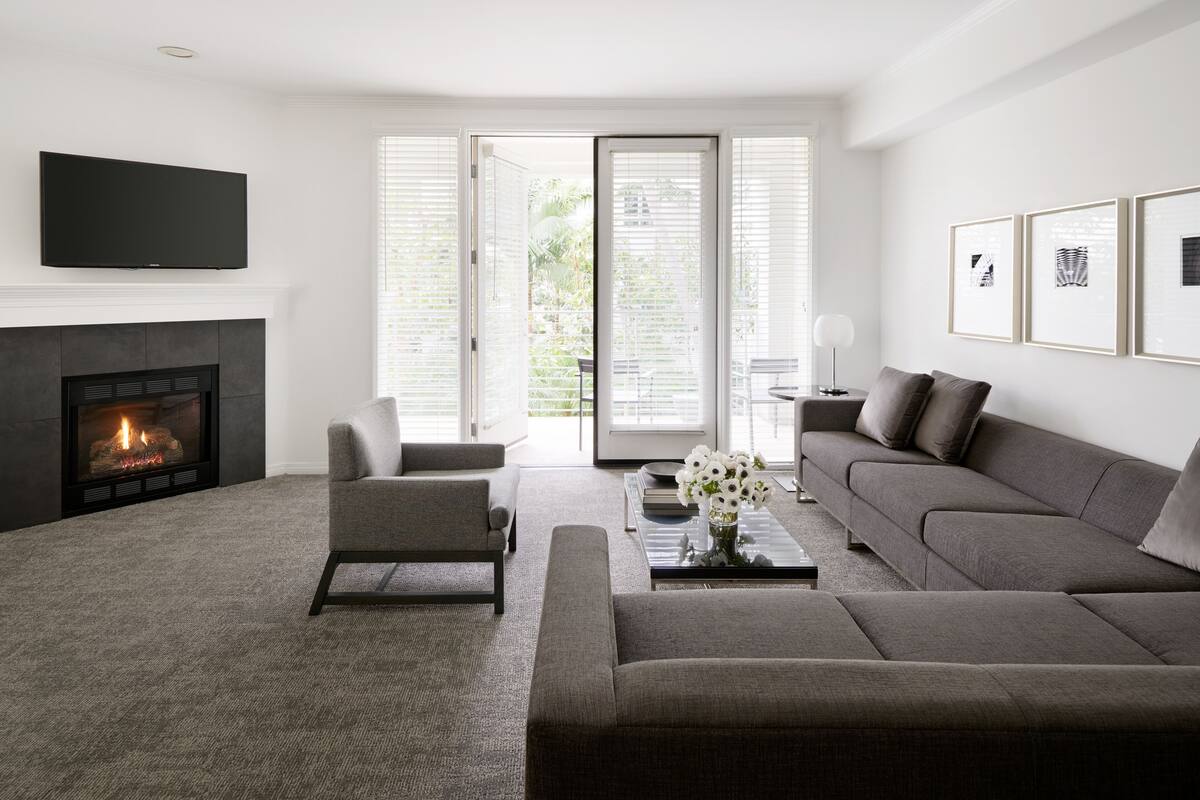 A modern living room with a fireplace, a grey sofa, a coffee table with a vase of flowers, and a television mounted on the wall.
