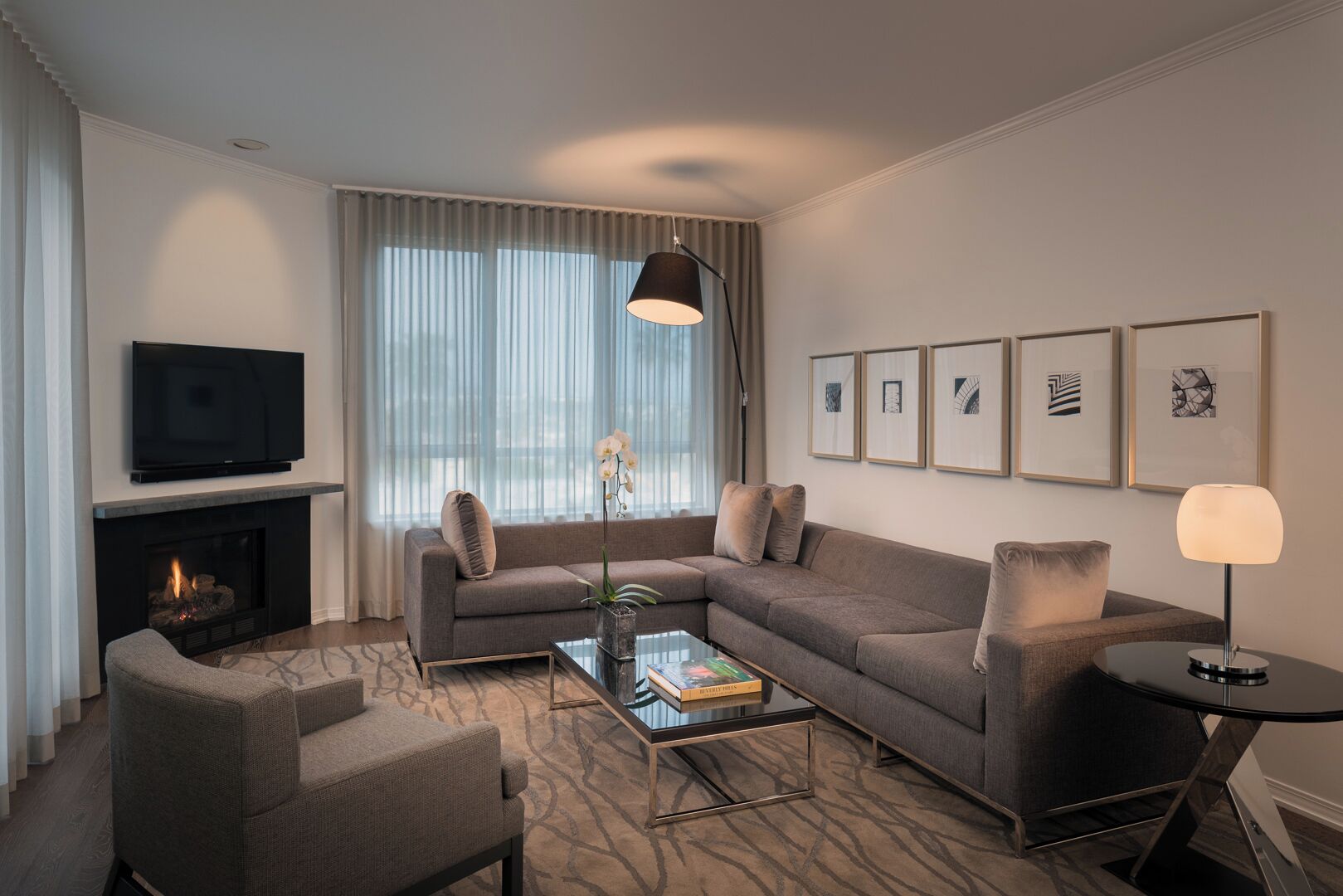 A modern living room with a sofa, armchair, coffee table, fireplace, TV, and artwork on the wall.