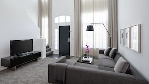 Un salon moderne avec un téléviseur à écran plat, un canapé, une table basse sur laquelle se trouvent un livre et un vase de fleurs, ainsi qu’un escalier menant à une autre pièce.