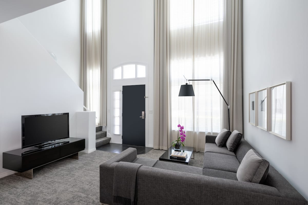 A modern living room with a flat-screen TV, a sofa, a coffee table with a book and a vase of flowers, and a staircase leading to another room.