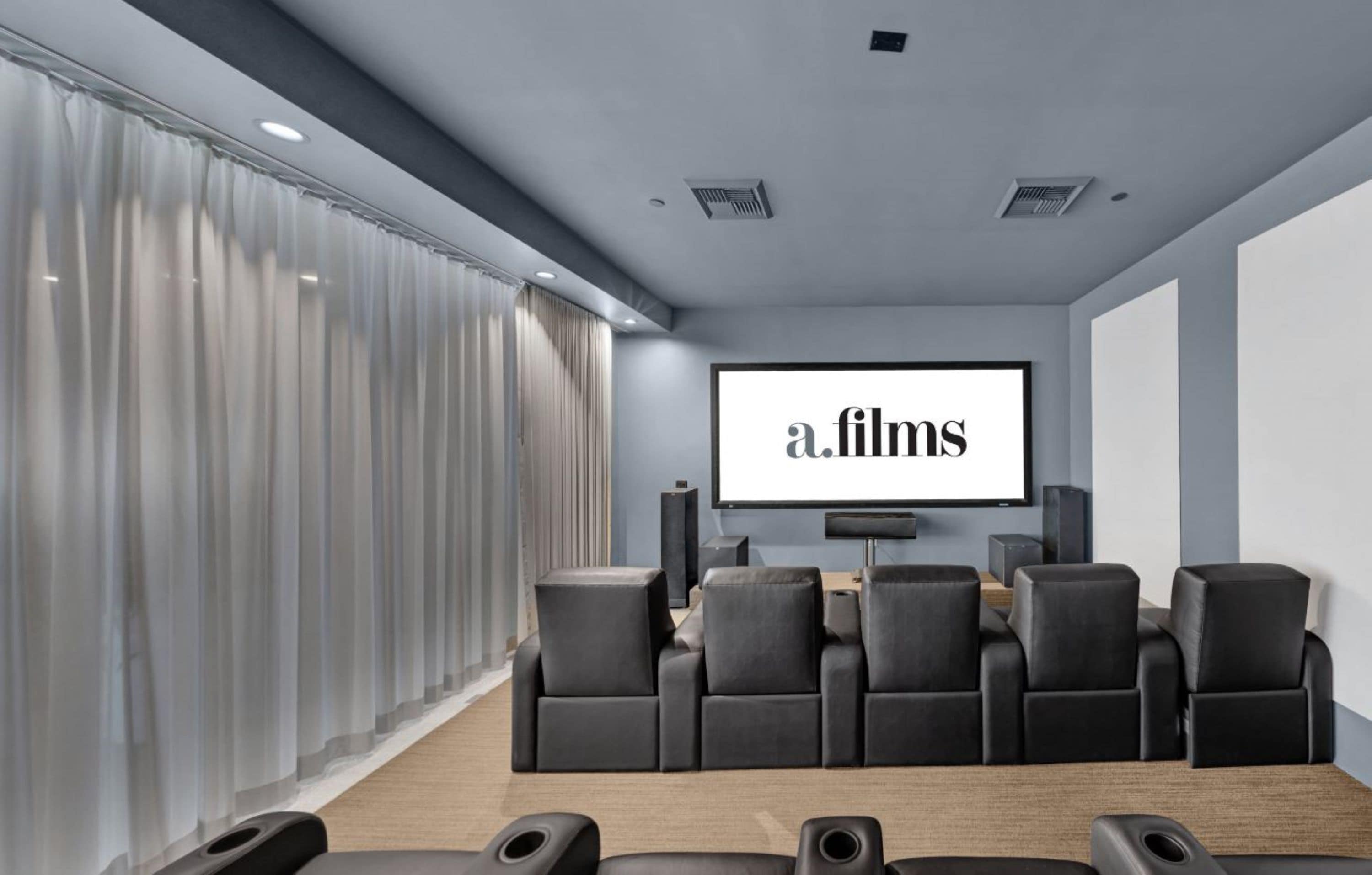 Un cine en casa moderno con una pantalla grande mostrando "a.films", asientos cómodos y un sistema de sonido.