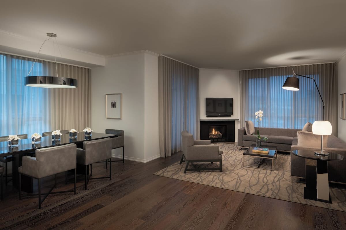 A modern living room with a fireplace, a dining area with a table and chairs, and a seating area with a sofa and armchairs.