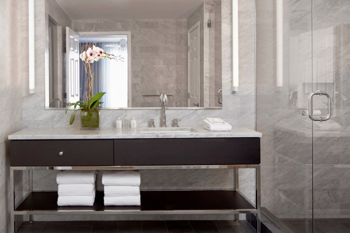 A modern bathroom with a marble sink, a glass shower enclosure, and a vase with flowers.