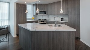 Une cuisine moderne dotée d’un îlot en marbre, d’appareils électroménagers en acier inoxydable et de luminaires suspendus.