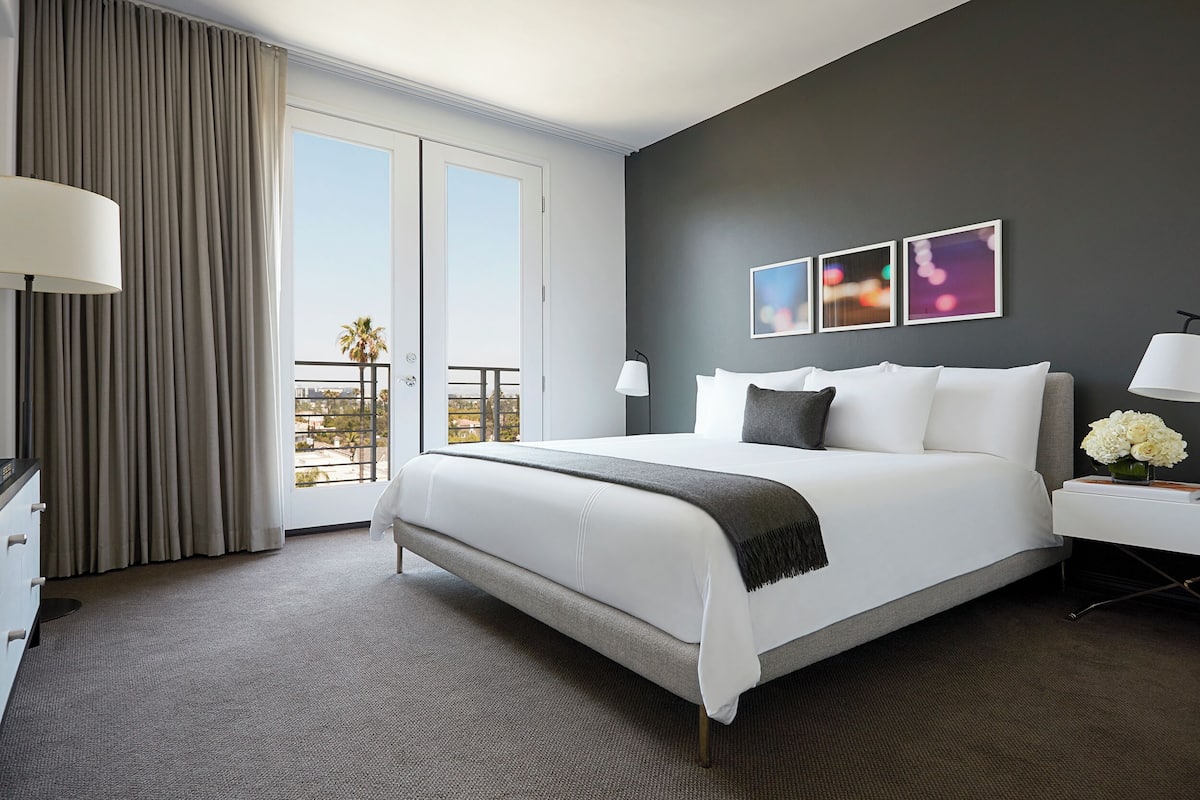 A modern hotel room with a large bed, a nightstand, a desk, and a view of the outdoors.