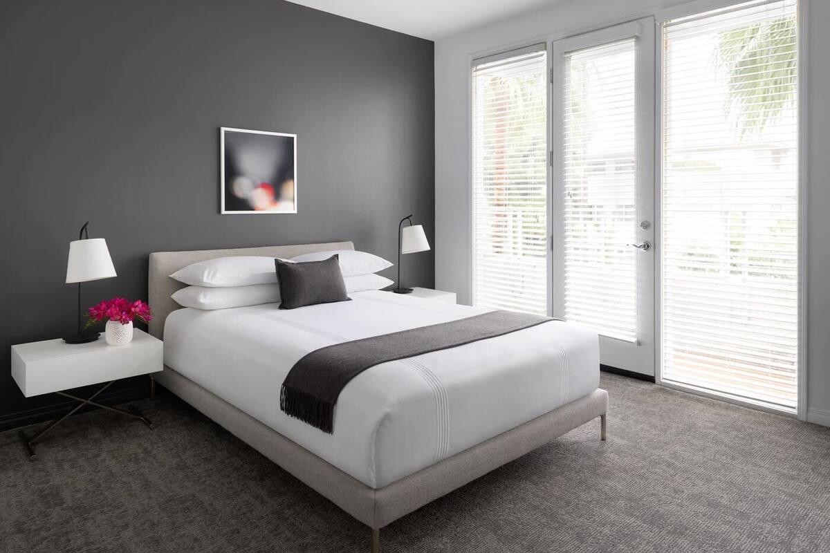 A modern bedroom with a large bed, two bedside tables, a nightstand, a picture on the wall, and a view through the window.
