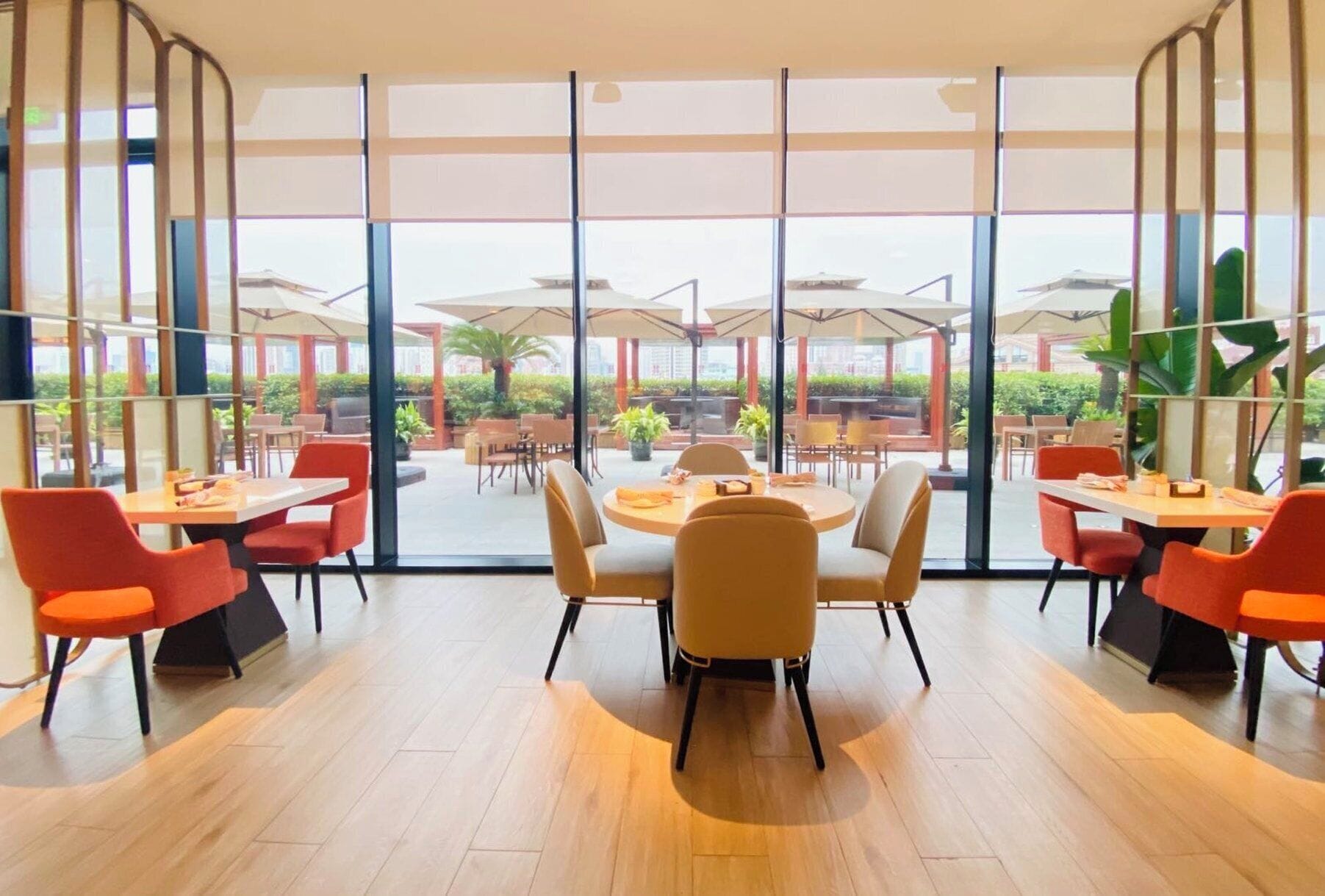 Un comedor moderno con grandes ventanales, suelo de madera y sillas color naranja.