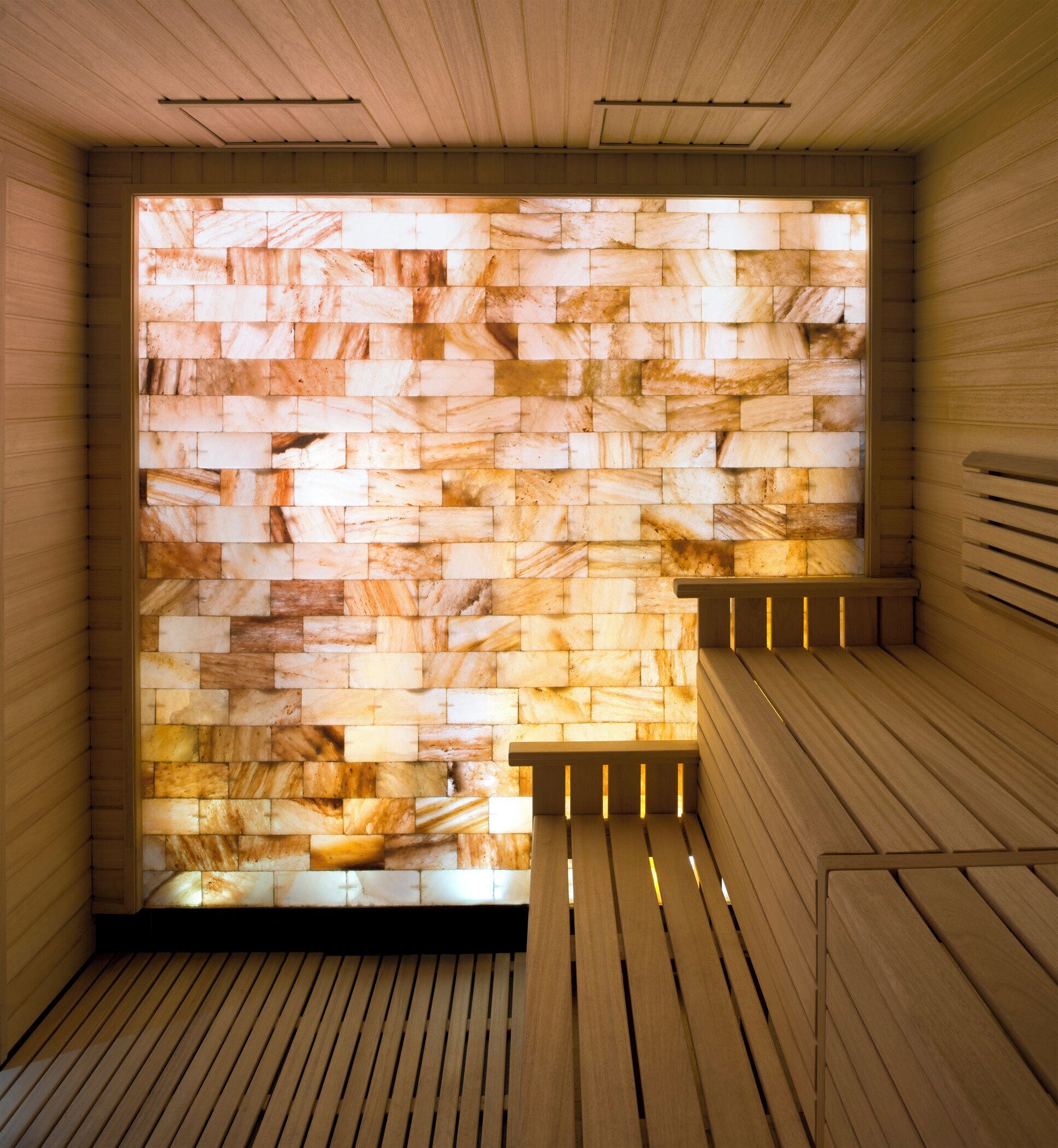 Una sauna con suelo y bancos de madera, que presenta una pared con un mosaico de baldosas de piedra.