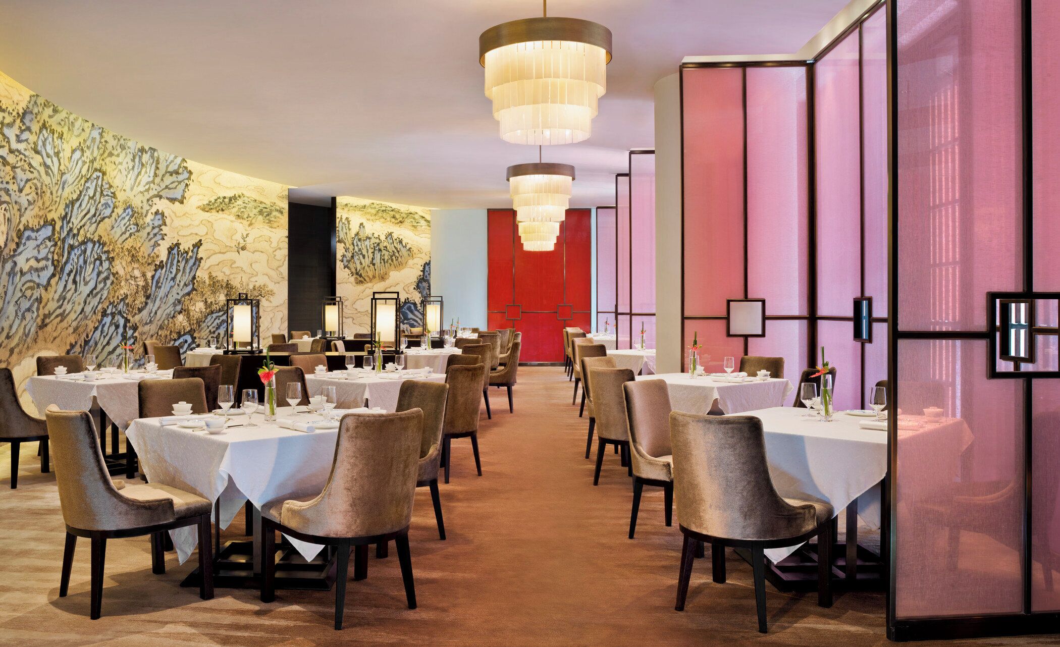 A dining area with tables set for service, a large mural on the wall, and a red accent wall.