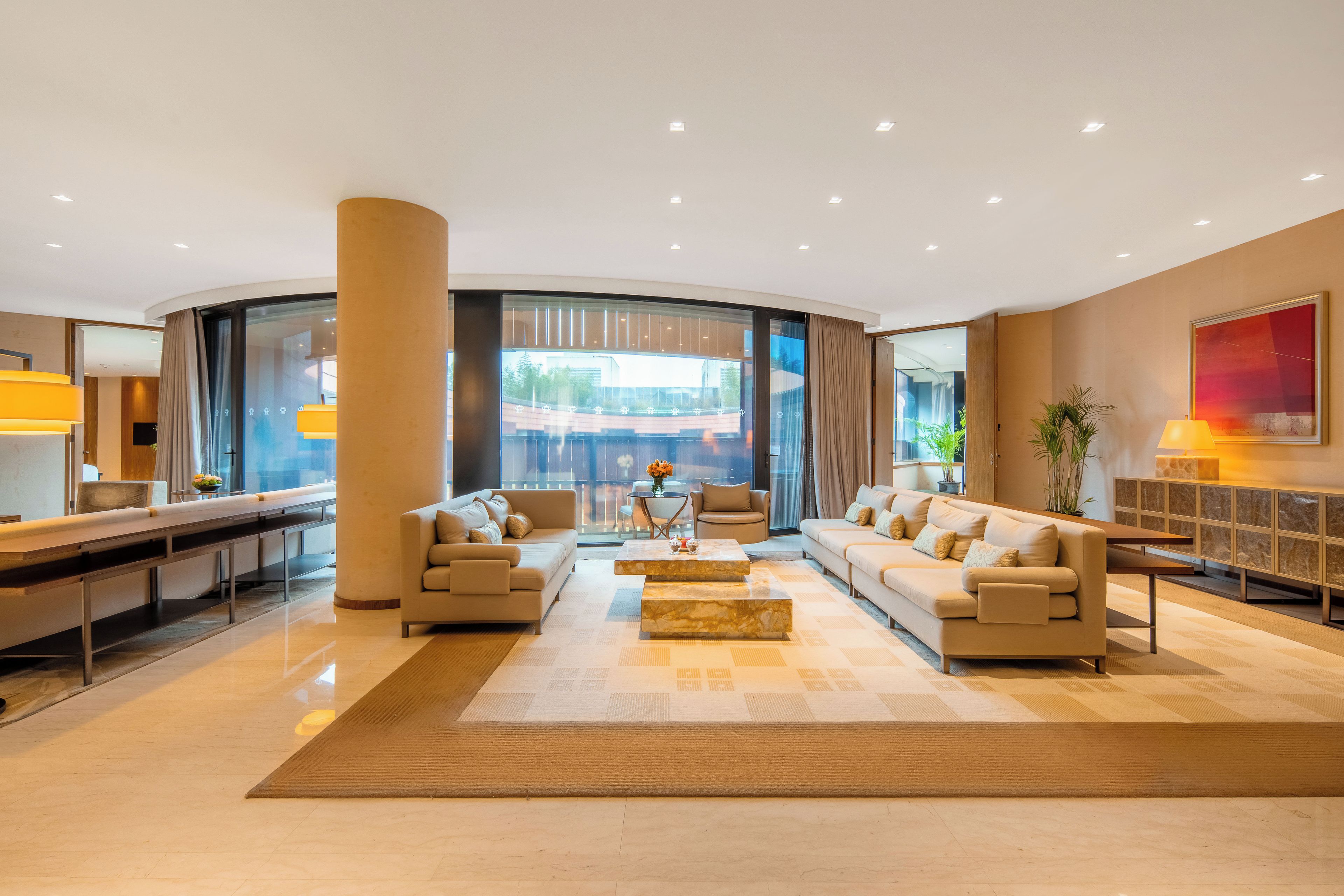 Una hall d'albergo moderna con una zona salotto a forma di curva, una reception e un'ampia finestra che offre vista all'esterno.