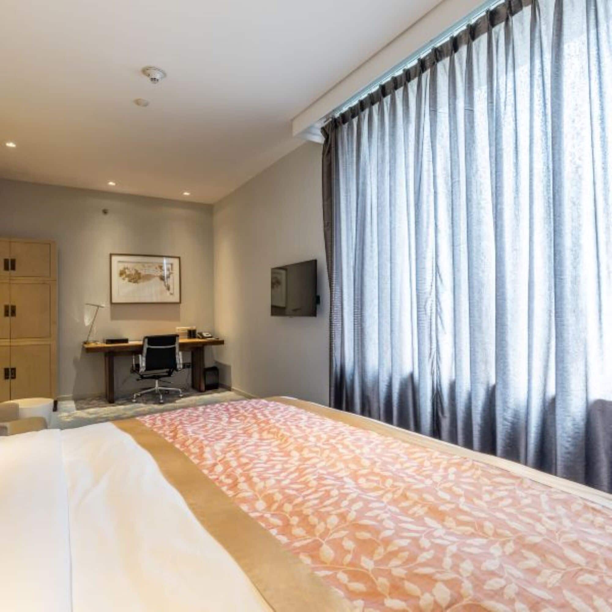 A hotel room with a bed, a desk, a chair, a television, and a wardrobe.
