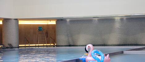 An indoor swimming pool with a pink flamingo float and a ladder in the background.