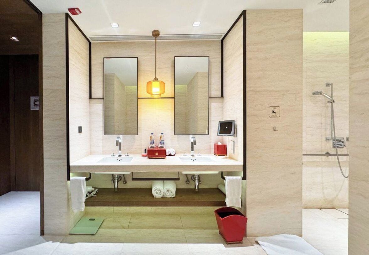 Uma casa de banho moderna com duas pias, um espelho grande, uma luminária suspensa e um chuveiro.