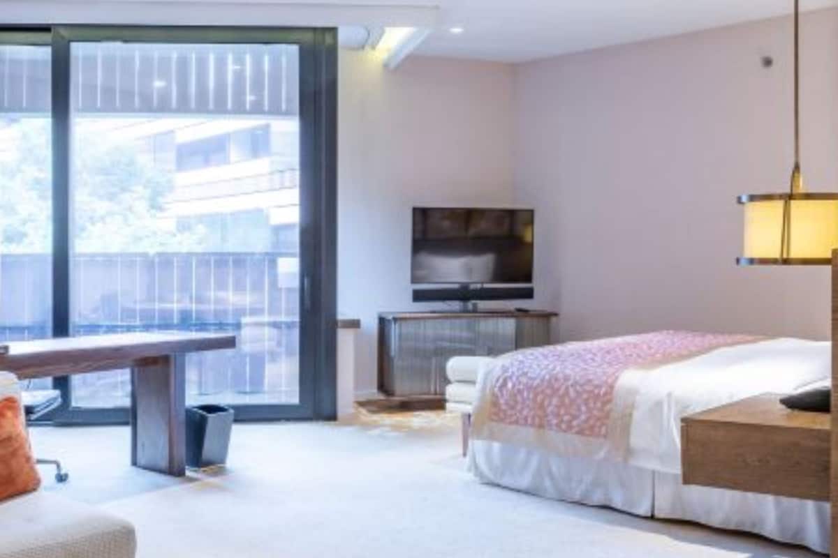 A modern bedroom with a large window, a bed, a bench, a TV, and a desk.