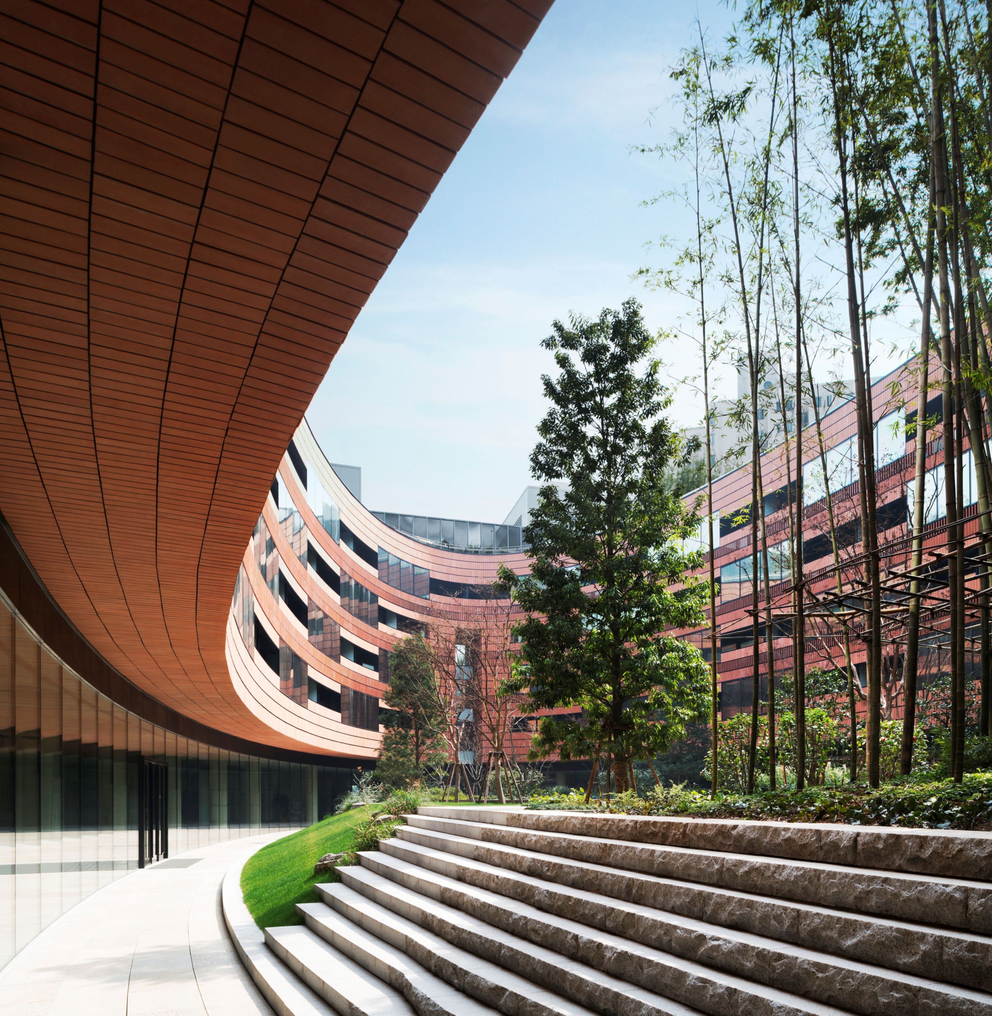 A modern building with a curved wooden facade, a staircase leading to a green lawn, and a clear sky.
