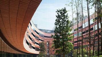 A modern building with a curved wooden facade, a staircase leading to a green lawn, and a clear sky.