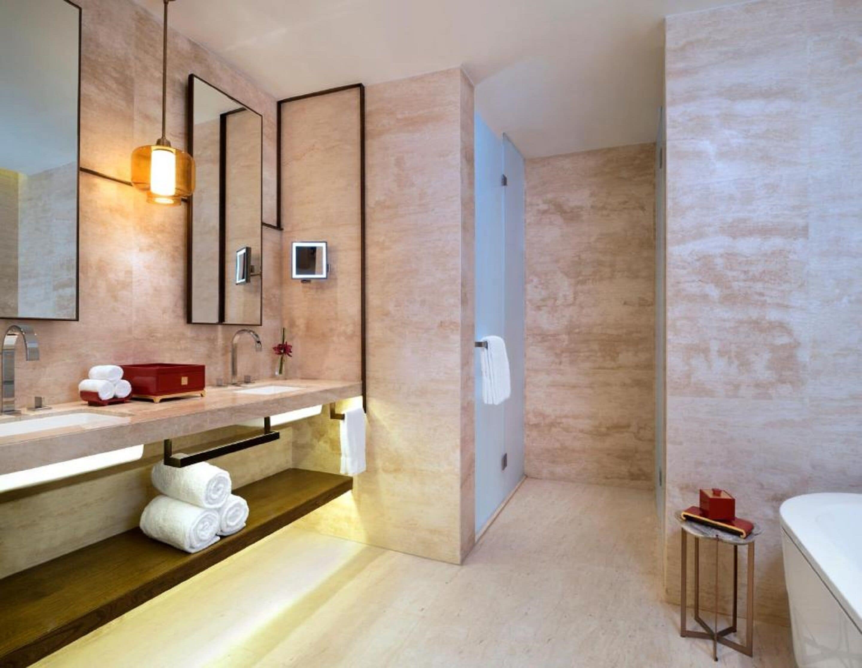 Un bagno moderno con uno specchio grande, un lavabo, una doccia e un tavolino con una scatola rossa.