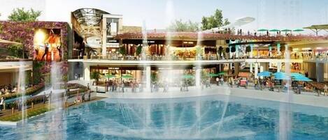A multi-level shopping mall with a central fountain, outdoor seating areas, and a variety of shops and restaurants.