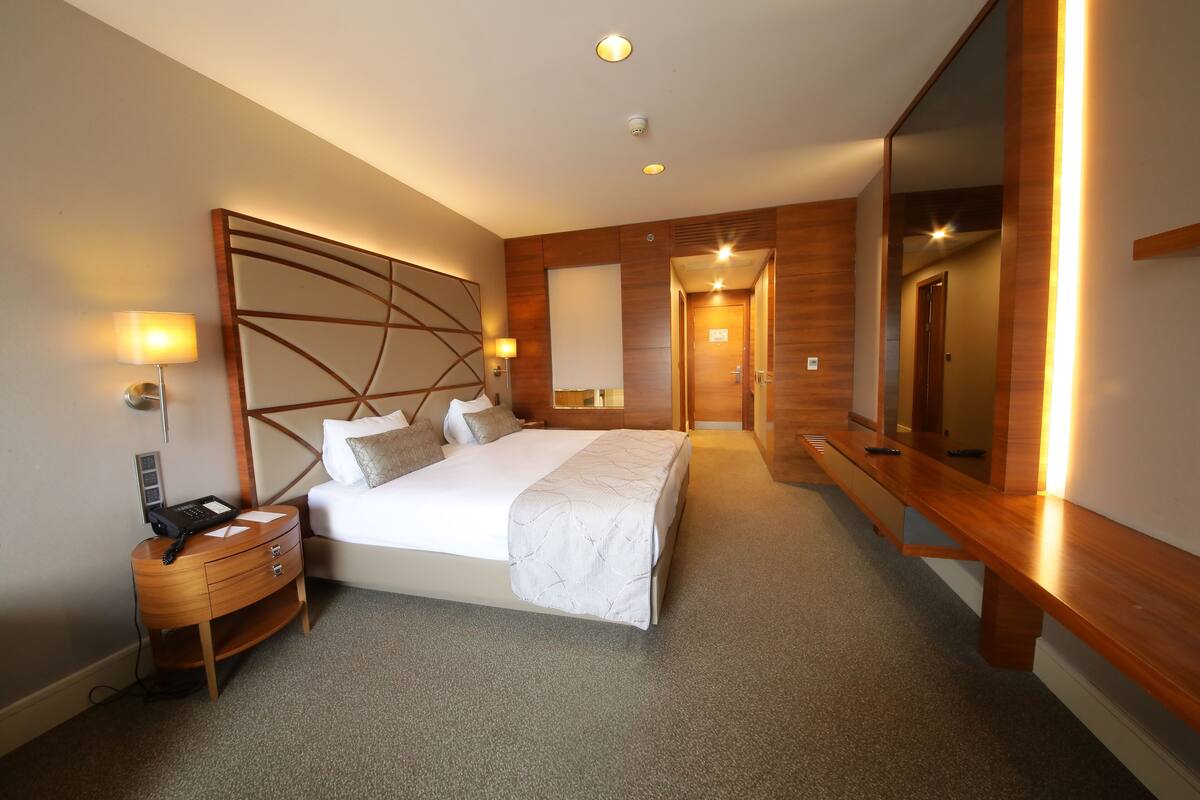 A modern hotel room with a large bed, bedside lamps, a wooden nightstand, and a large mirror.
