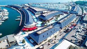 An aerial view of a marina with boats docked, a large swimming pool, and a covered area with umbrellas.
