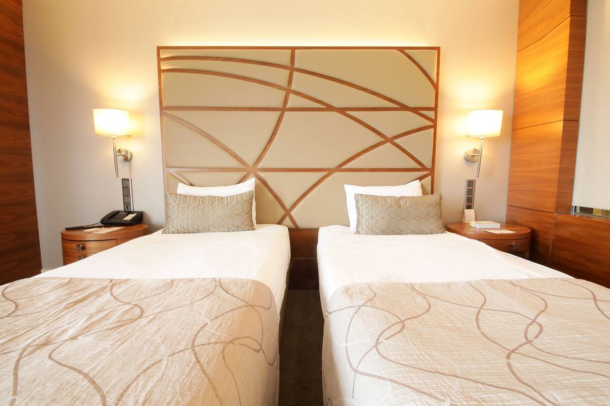 A hotel room with two beds, each with a headboard, bedside tables, lamps, and a phone.