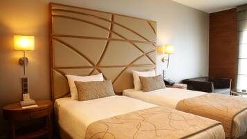 A hotel room with two beds, a wooden headboard, bedside lamps, a desk, and a chair.