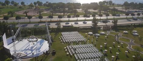 Un espacio para eventos al aire libre con escenario y zona de estar, rodeado de vegetación y vistas al mar.