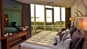 A hotel room with a large bed, a sitting area with a table and chairs, a large window with a view of the city, and a mirror on the wall.