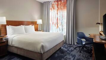 A hotel room with a large bed, two bedside lamps, a desk with a chair, and a window with curtains.