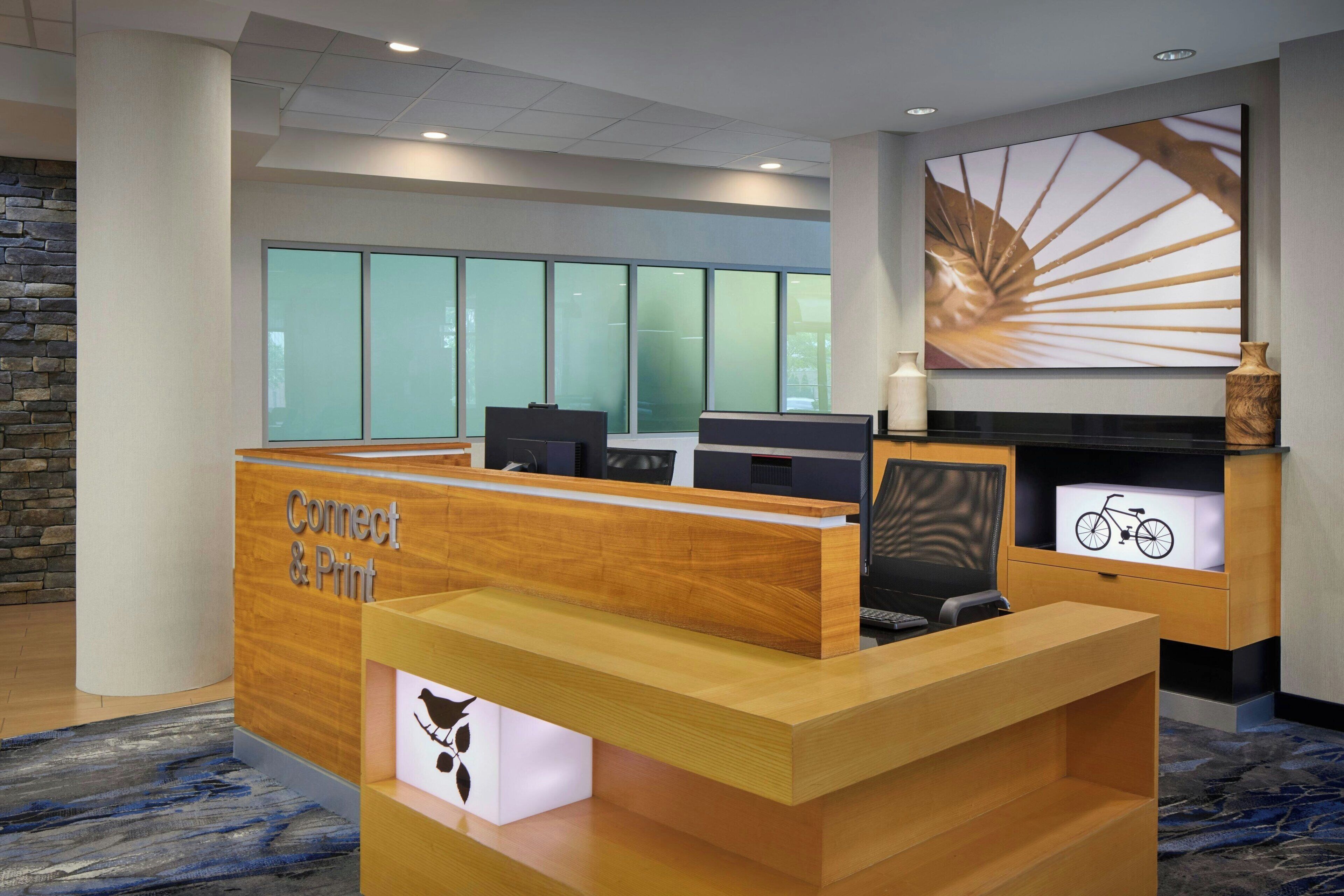 A reception desk with a 'Connect & Print' sign, a large window with a view, and a wall-mounted artwork.