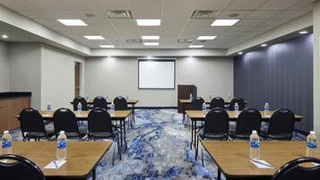 Un salón de conferencias con mesas, sillas y una pantalla para proyector.