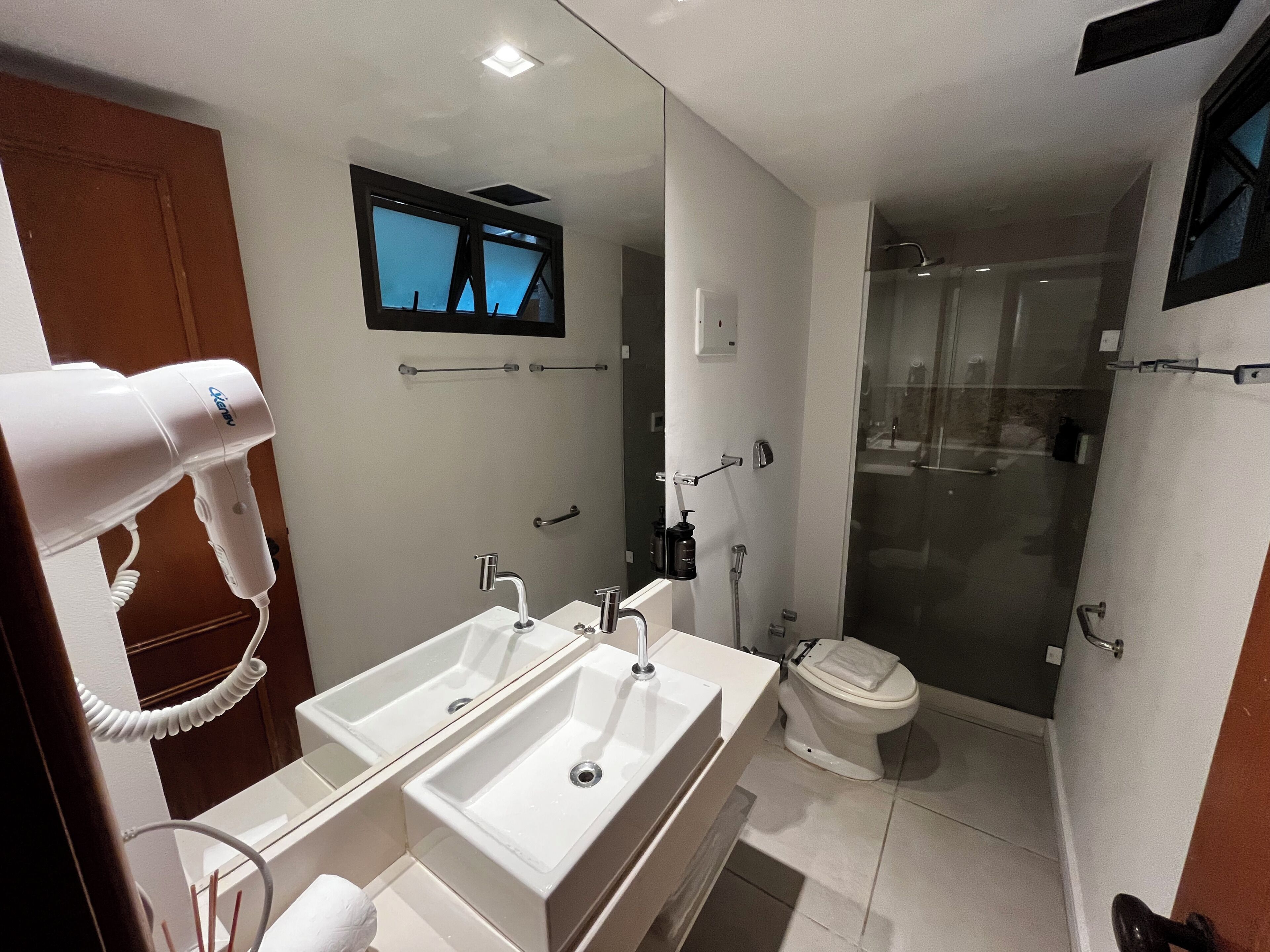 Une salle de bain moderne dotée de deux lavabos, d’un sèche-cheveux, d’un miroir, de toilettes et d’une cabine de douche en verre.